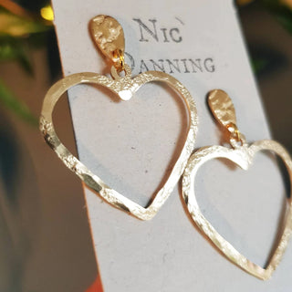 Glowing gold earrings in statement cutout heart design. 'The Lovers, Portia' ethical hand beaten brass earrings by Nic Danning Jewellery.
