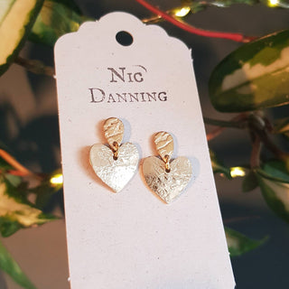 Glowing gold stud earrings in dainty heart design. 'The Lovers, Rosalind' ethical hand beaten brass earrings by Nic Danning Jewellery.