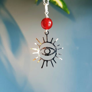 Charity fundraiser design to support the humanitarian crisis in Syria. Shimmering silver necklace with eye of protection design and carnelian bead. 'Himaya' ethical hand beaten stainless steel necklace by Nic Danning Jewellery.