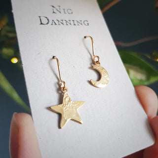 Glowing gold earrings in tiny mismatched star and crescent moon design. 'Tempest Stella Luna' ethical hand beaten brass earrings by Nic Danning Jewellery.