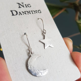 Shimmering silver earrings in tiny mismatched star and crescent moon design. 'Tempest Stella Luna' ethical hand beaten stainless steel earrings by Nic Danning Jewellery.