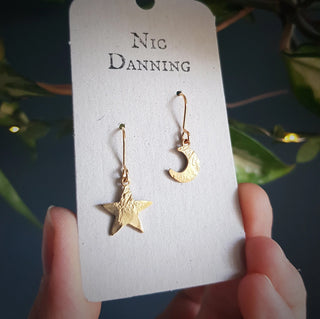 Glowing gold earrings in tiny mismatched star and crescent moon design. 'Tempest Stella Luna' ethical hand beaten brass earrings by Nic Danning Jewellery.