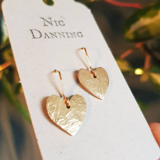 Glowing gold earrings in dainty heart design. 'The Lovers, Rosalind' ethical hand beaten brass earrings by Nic Danning Jewellery.