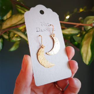Glowing gold earrings in dainty crescent moon design. 'Gossamer Demi Lune' ethical hand beaten brass earrings by Nic Danning Jewellery.