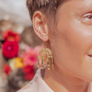 Glowing gold earrings in statement hanging arcs design. 'Tempest Rainbow' ethical hand beaten brass earrings by Nic Danning Jewellery.