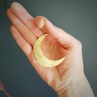 Glowing gold earrings in statement crescent moon design. 'Tempest Artemis' ethical hand beaten brass earrings by Nic Danning Jewellery.