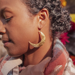 Glowing gold earrings in statement crescent moon design. 'Tempest Artemis' ethical hand beaten brass earrings by Nic Danning Jewellery.