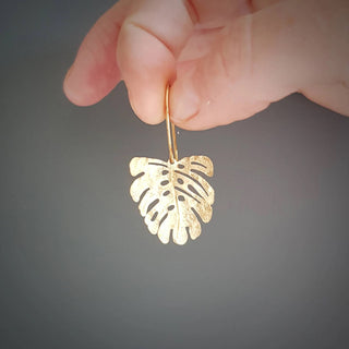 Glowing gold earrings in a dainty monstera leaf design. 'Tempest Tropic' ethical hand beaten brass earrings by Nic Danning Jewellery.