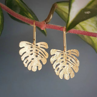 Glowing gold earrings in a dainty monstera leaf design. 'Tempest Tropic' ethical hand beaten brass earrings by Nic Danning Jewellery.