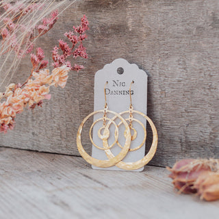 Glowing gold earrings in statement concentric hoop design. 'Tempest Saturn' ethical hand beaten brass earrings by Nic Danning Jewellery.