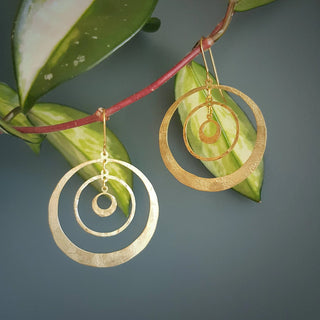 Glowing gold earrings in statement concentric hoop design. 'Tempest Saturn' ethical hand beaten brass earrings by Nic Danning Jewellery.
