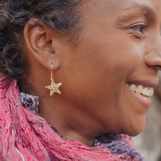 Glowing gold earrings in asymmetric star and crescent moon design. 'Tempest Stella Luna' ethical hand beaten brass earrings by Nic Danning Jewellery.