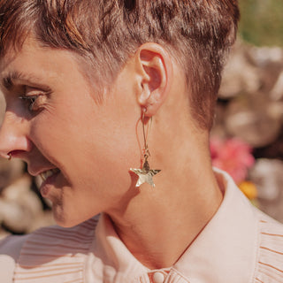 Glowing gold drop earrings in statement star design. 'Tempest Supernova' ethical hand beaten brass earrings by Nic Danning Jewellery.