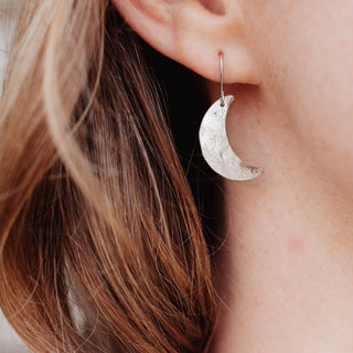 Shimmering silver earrings in dainty crescent moon design. 'Gossamer Demi Lune' ethical hand beaten stainless steel earrings by Nic Danning Jewellery.
