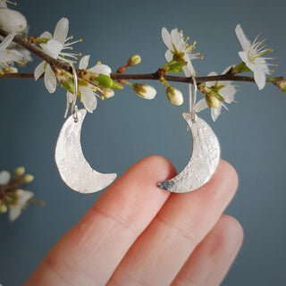 Shimmering silver earrings in dainty crescent moon design. 'Gossamer Demi Lune' ethical hand beaten stainless steel earrings by Nic Danning Jewellery.