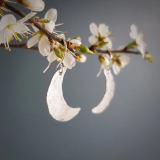 Shimmering silver earrings in dainty crescent moon design. 'Gossamer Demi Lune' ethical hand beaten stainless steel earrings by Nic Danning Jewellery.