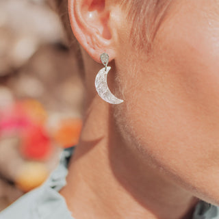 Shimmering silver stud earrings in dainty crescent moon design. 'Gossamer Demi Lune' ethical hand beaten stainless steel earrings by Nic Danning Jewellery.