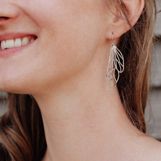 Shimmering silver earrings in cutout dragonfly wing design. 'Gossamer Dryad' ethical hand beaten stainless steel earrings by Nic Danning Jewellery.