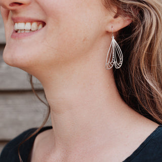 Shimmering silver earrings in cutout dragonfly wing design. 'Gossamer Naiad' ethical hand beaten stainless steel earrings by Nic Danning Jewellery.