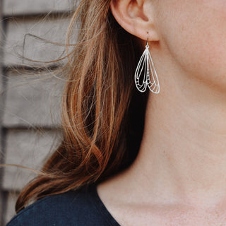 Shimmering silver earrings in cutout dragonfly wing design. 'Gossamer Naiad' ethical hand beaten stainless steel earrings by Nic Danning Jewellery.